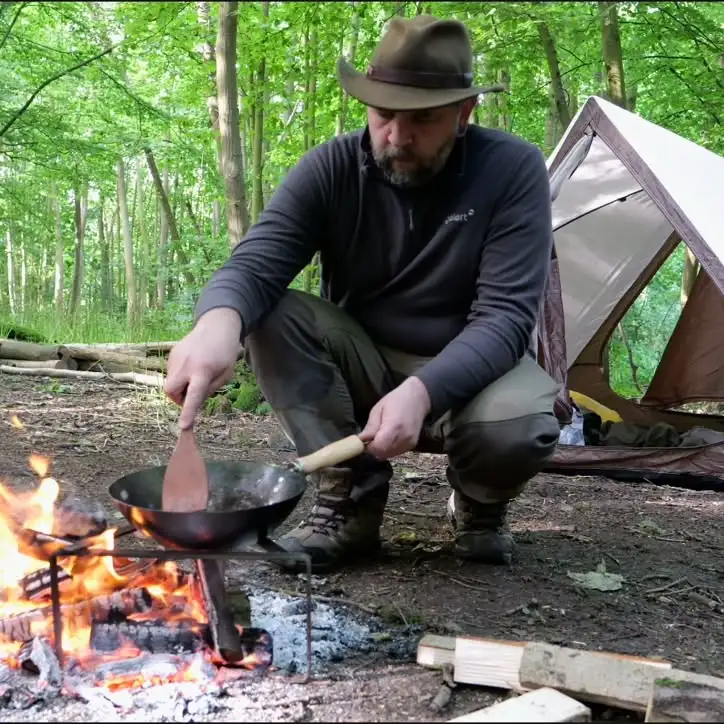 Andrew Davidson, aka Kent Survival, cooking over a campfire in the woods during a solo bushcraft camping trip.