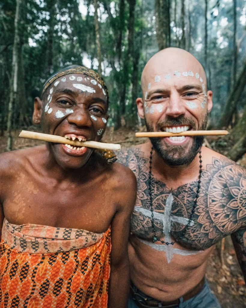 Travel vlogger Mike Corey with the Baka Pygmies in Cameroon, experiencing traditional tribal life with face paint and cultural rituals